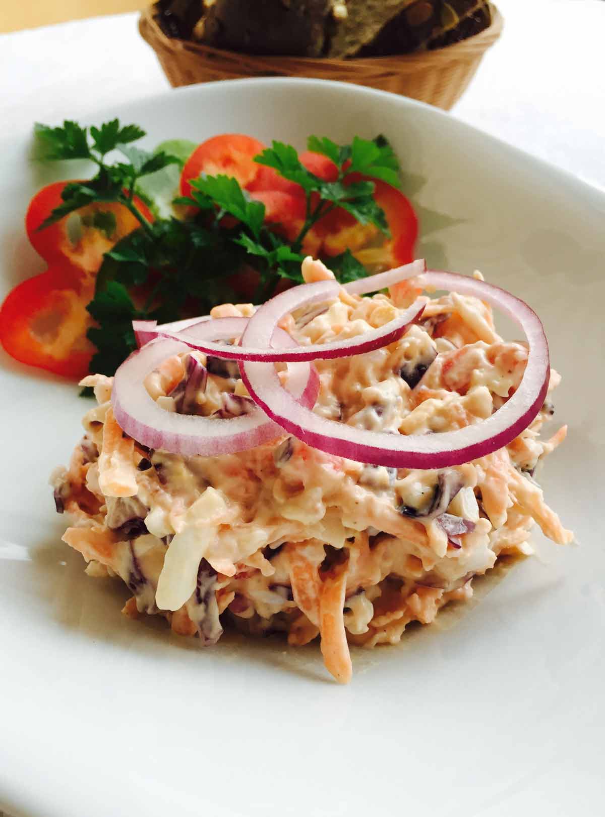 A coleslaw with egg, red cabbage and carrots, on a white plate, with onion rings