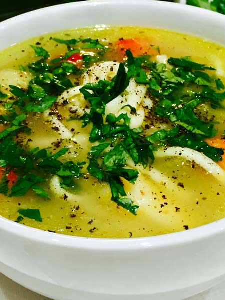 A close-up of a tasty and comforting chicken soup, in a white plate.