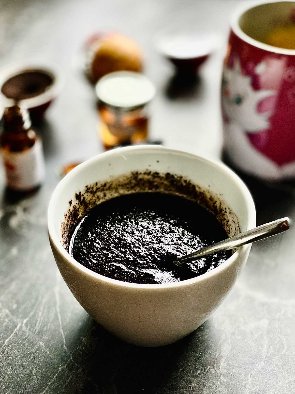 Coffee scrub close up in a white ceramic dish with a mixing teaspoon in with blurred background