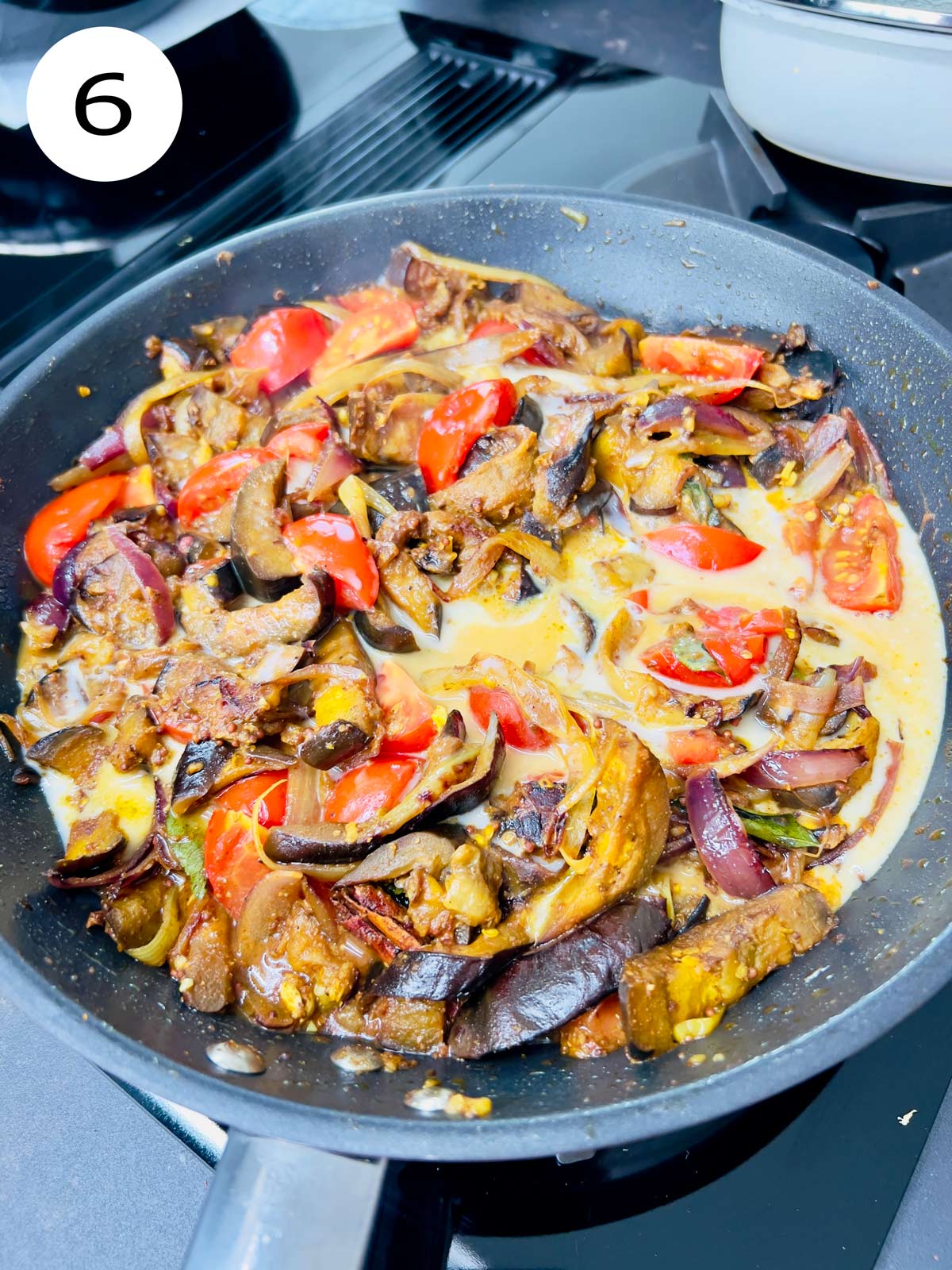 Coconut milk added to the aubergine curry cooking in a pan.