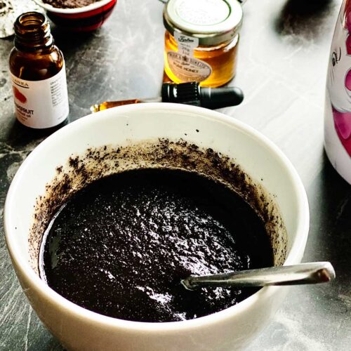 DIY cofee scrub in a white ceramic pot placed on a dark marbled surface and a tiny honey jar and coffee pods at the top