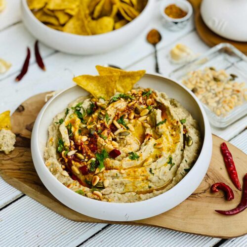 Creamy eggplant dip spread in a fancy deep plate placed on a wooden board and red chillies on the side