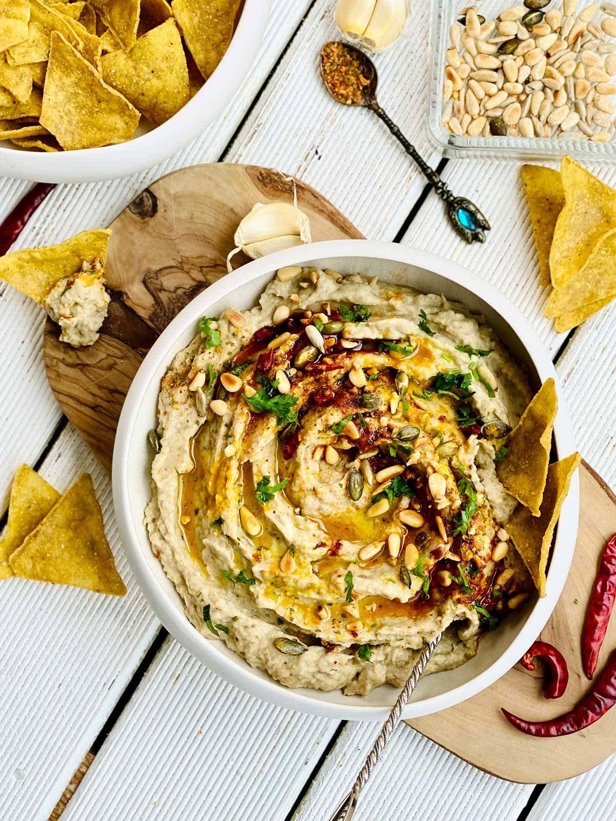 Creamy eggplant dip spread birdsview in an ivory deep plate placed on a wooden board with red chillies and tortilla chips scattered around the sides