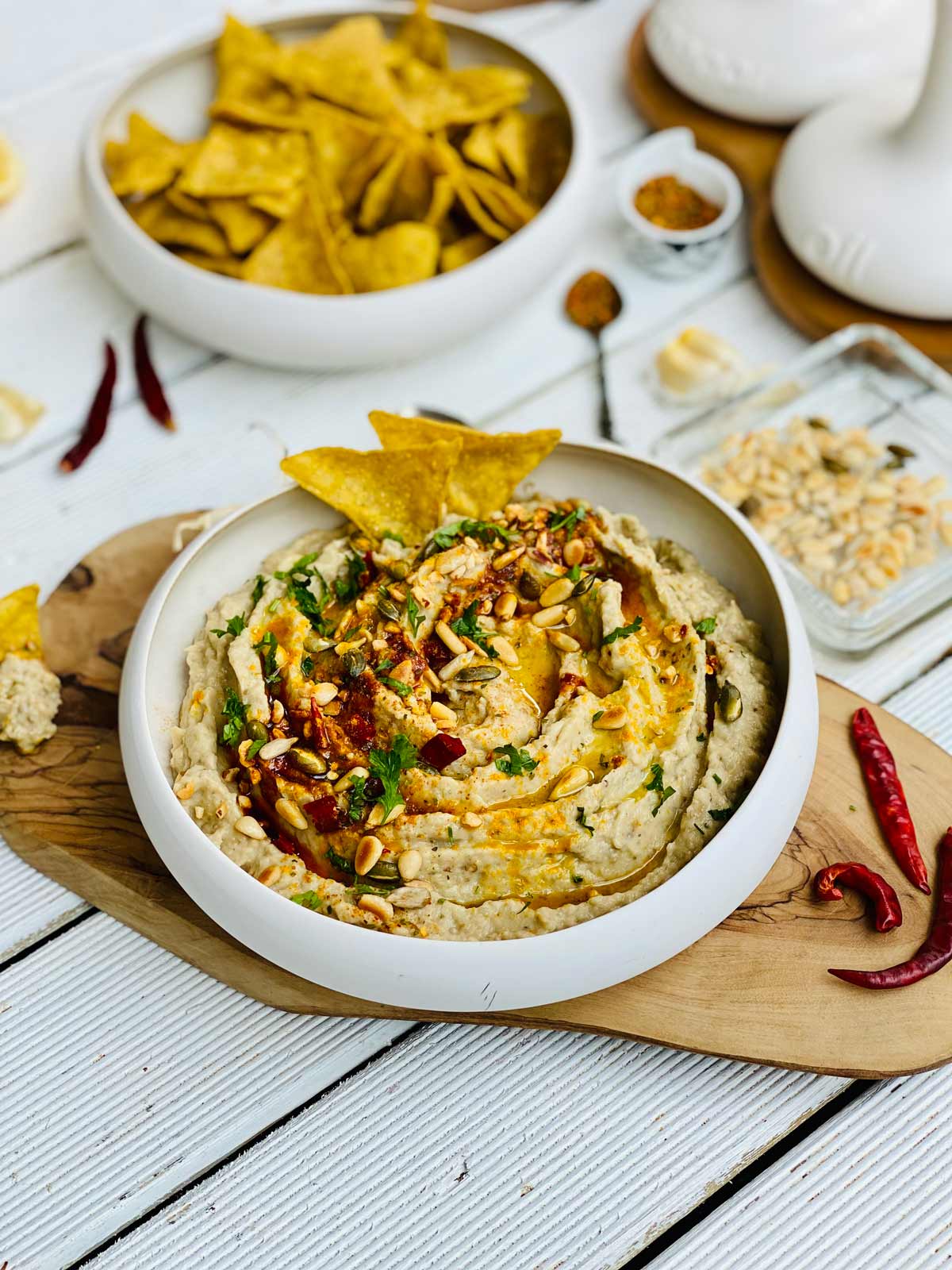 Creamy eggplant dip spread in a fancy deep plate placed on a wooden board and red chillies on the side