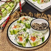 Cucumber roll slices on white plates with mixed sesame seeds sprinkled on top.