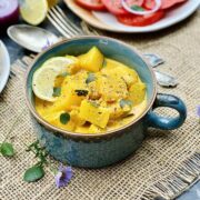 Pineapple curry in a green ceramic pot sprinkled with black pepper and curry leaves