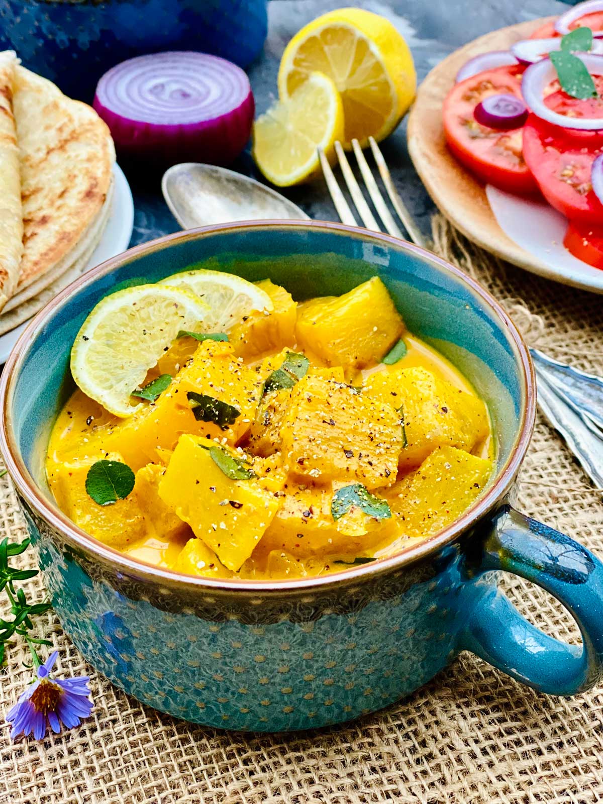 Closeup of pineapple curry in a nice green ceramic serving dish topped with two lemon slices and a sprinkle of black pepper