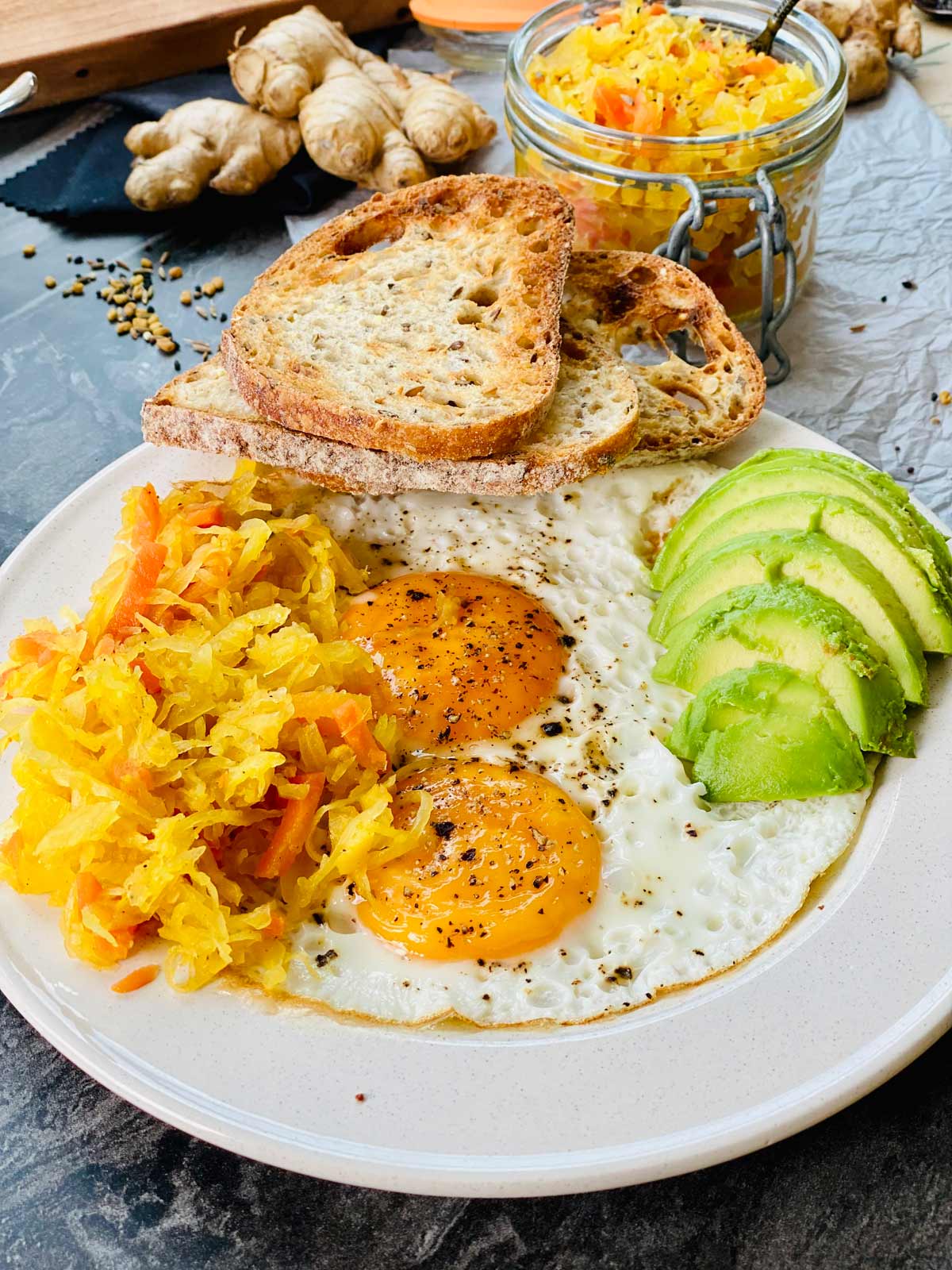 Two sunny side up eggs with avocado and toasted rustic bread and sauerkraut on a white ceramic plate