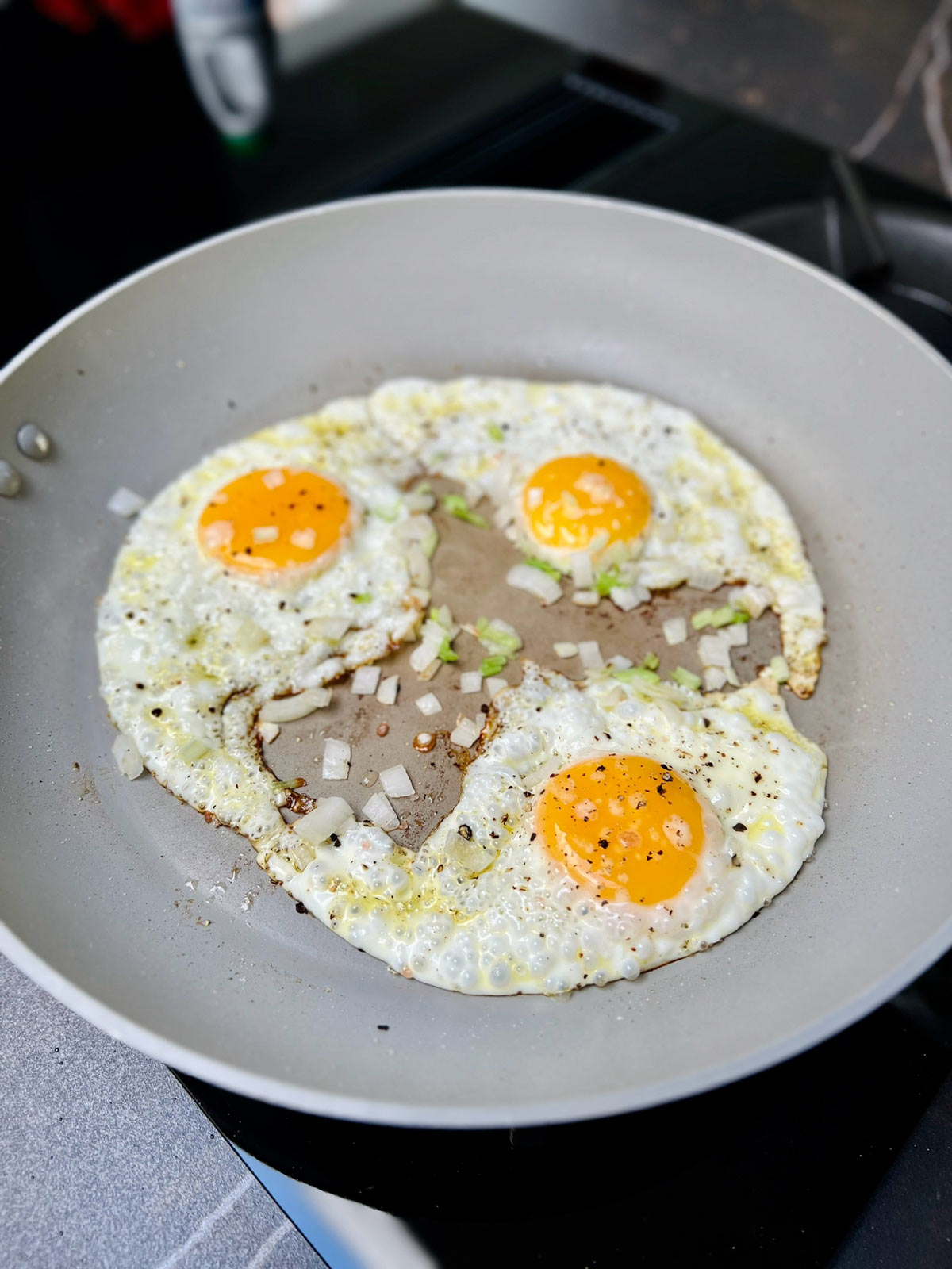 Three sunnyside up eggs cooked in a pan with sauteed onions/scallions.