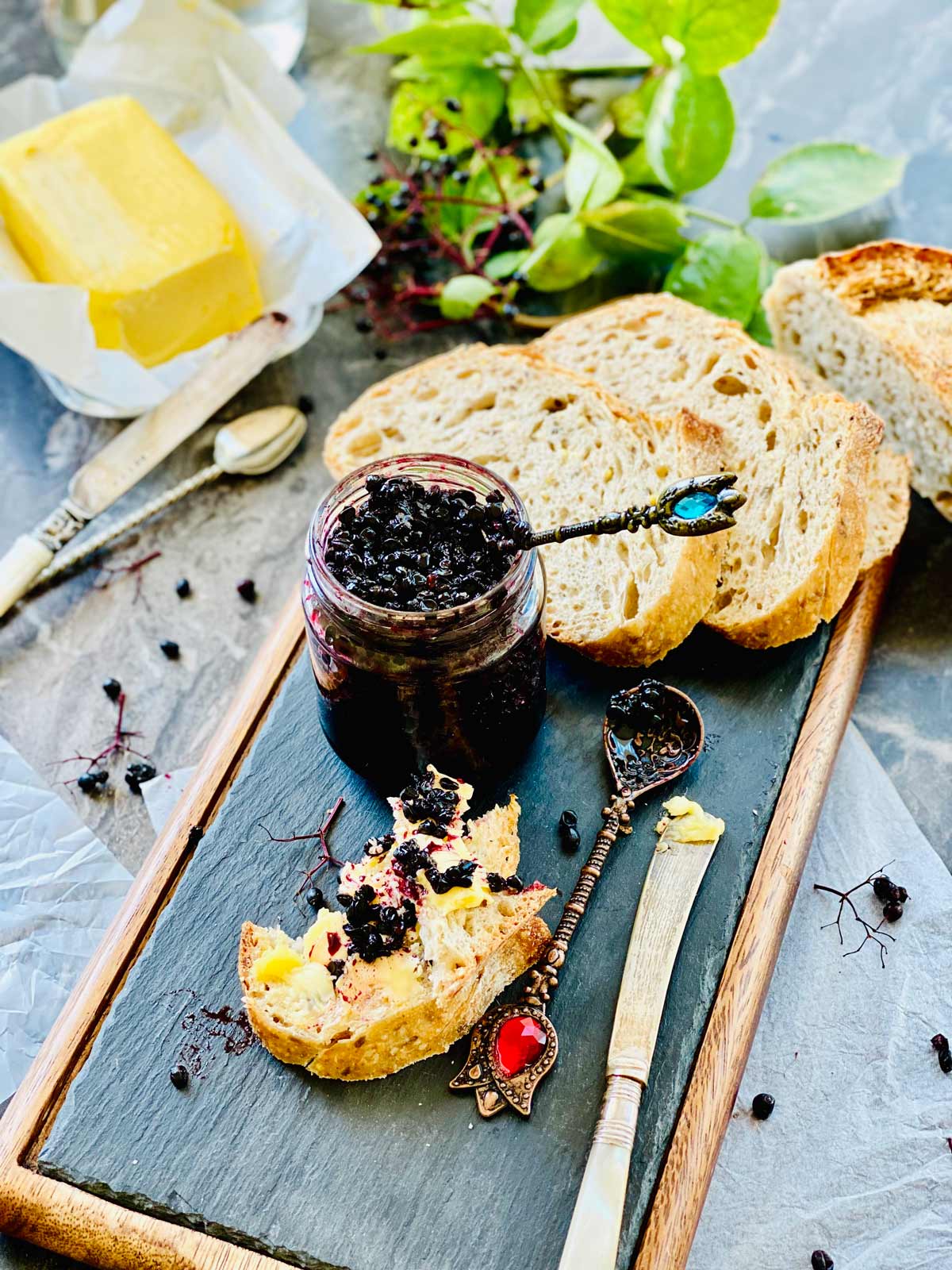 Elderberry jam, and a few slices of bread on a wooden board and a block of butter at the top.