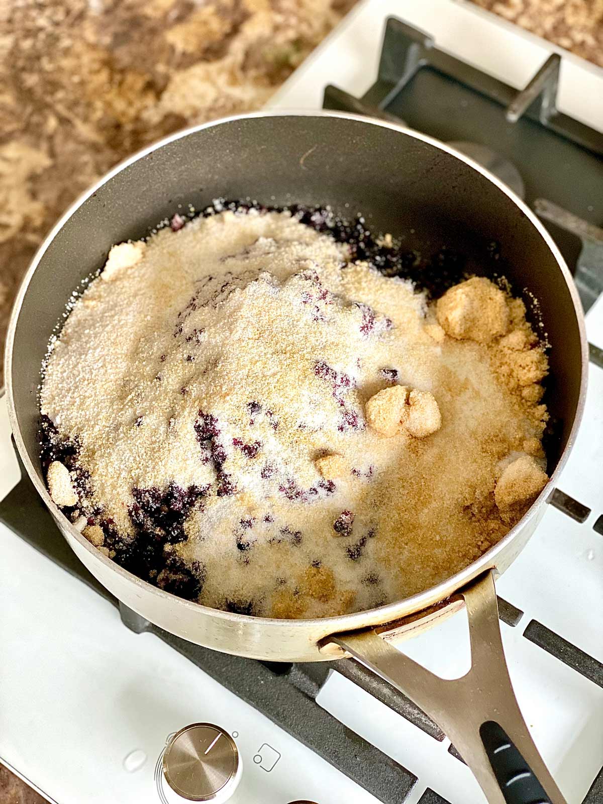Fresh elderberries in a pan topped with cane sugar on a stove.