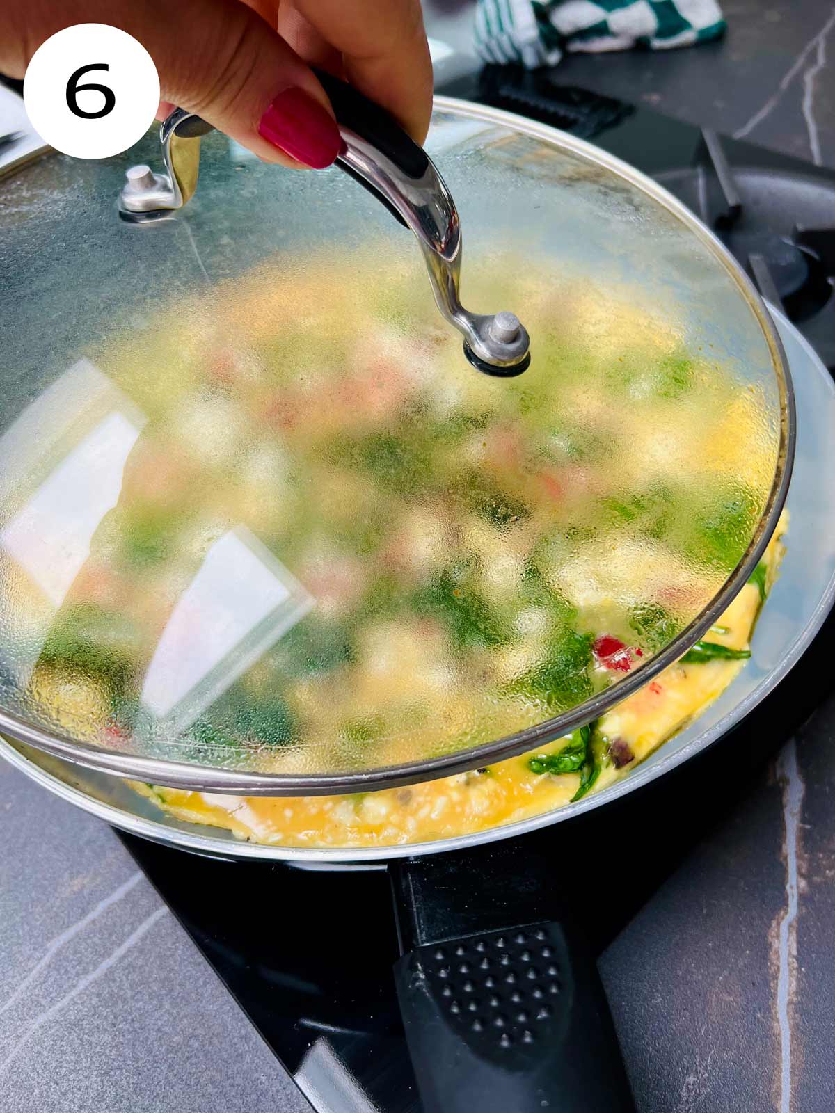 Feta and spinach omelette cooking in a pan with the lid being removed.