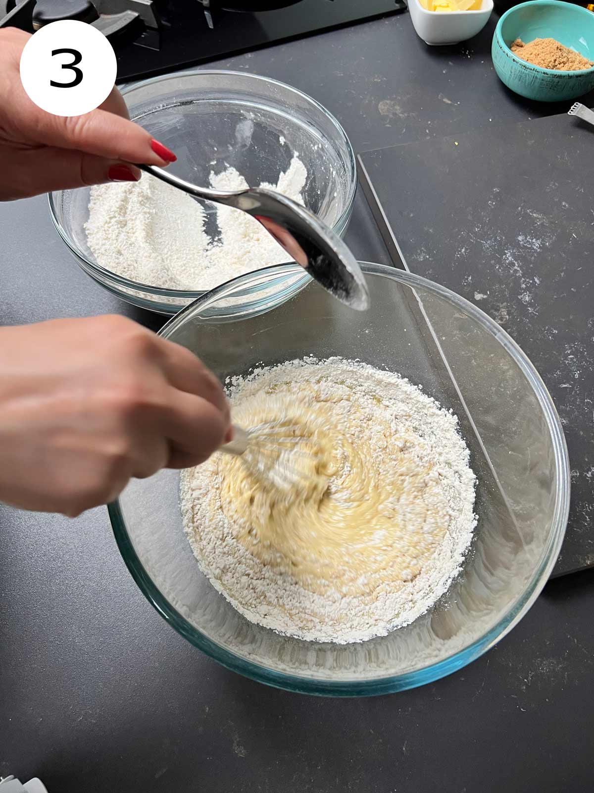 Flour being added to the egg mixture with a metal spoon.