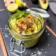 Close-up of avocado mayo topped with red chilli flakes, oregano top, mixed pepper grounded and a drizzle of olive oil.