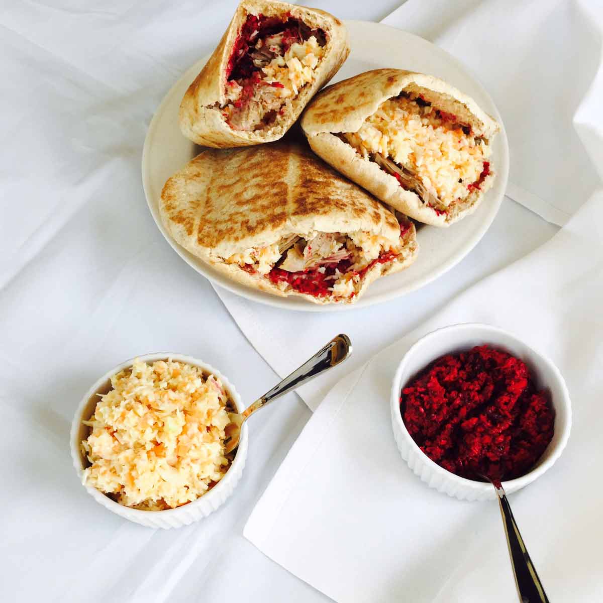 Three lamb pita pockets (sandwiches), alongside bowls of coleslaw and horseradish sauce