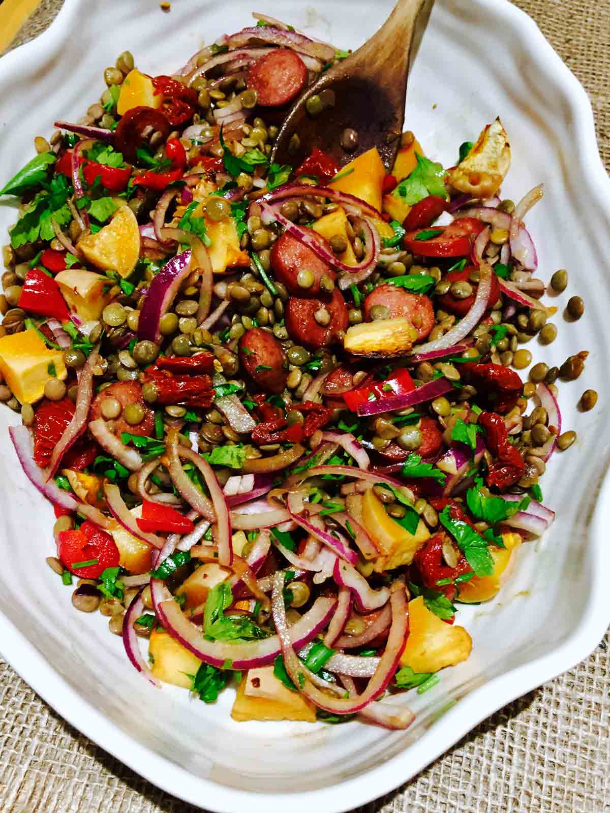 A white bowl of chunky lentils, chorizo and sun-dried tomatoes, ready to go.