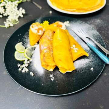 Three whole mango pancakes and two halves arranged nicely on a black ceramic serving plate with powdered sugar.