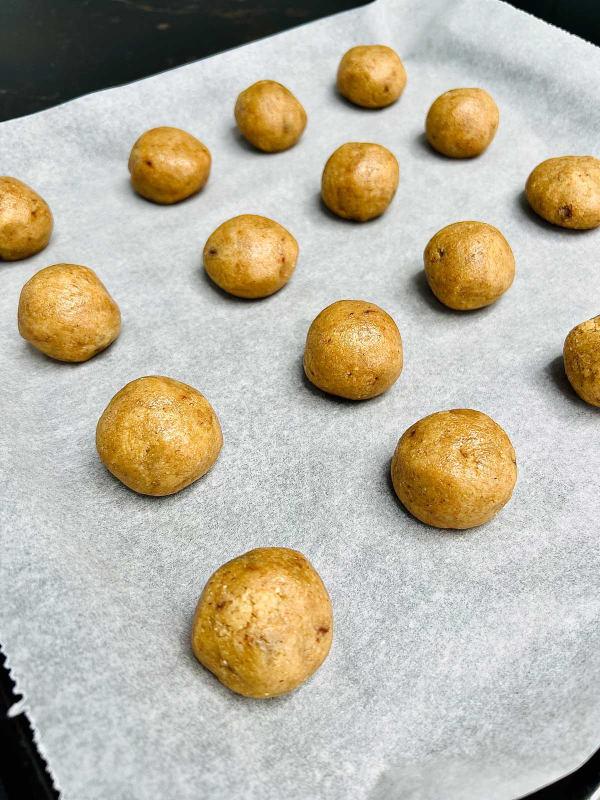 Raw, oat flour cookies balls lined on parchment paper in an oven tray ready to go in the oven.