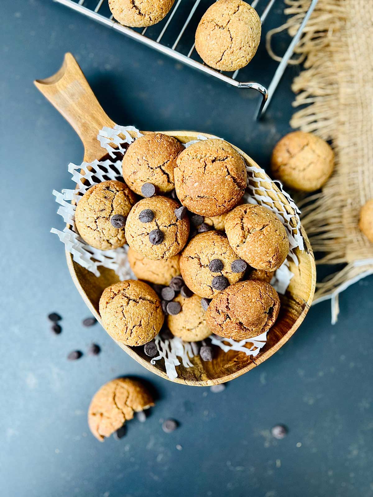 Oat flour cookies in a wooden serving dish sprinkled of chocolate chips and a few cookies and chips scattered around.