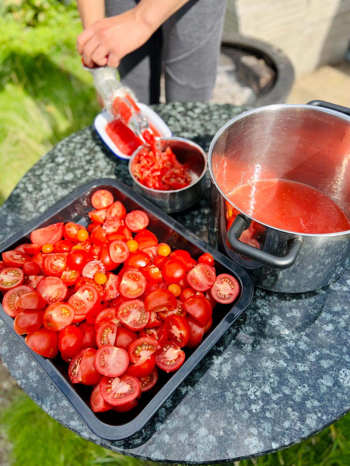 Passata di pomodoro in the making - a large stainless steel pot with a small amount of passata di pomodoro and a tray with chopped tomatoes.