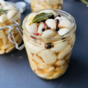Pickled garlic jars on a dark gray worktop topped with spices and bay leaves.