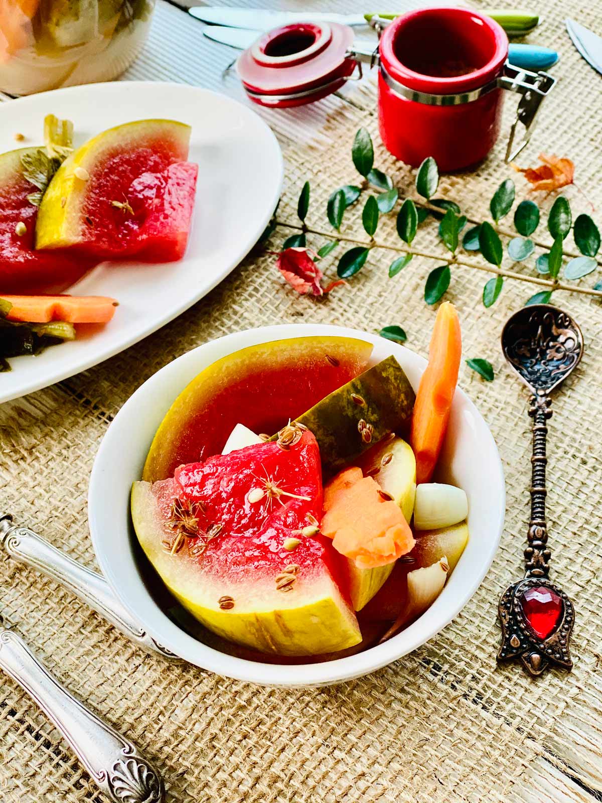 Pickled watermelon slices with pickled carrot in a white serving dish and a few more slices at the back top left side in an oval white plate