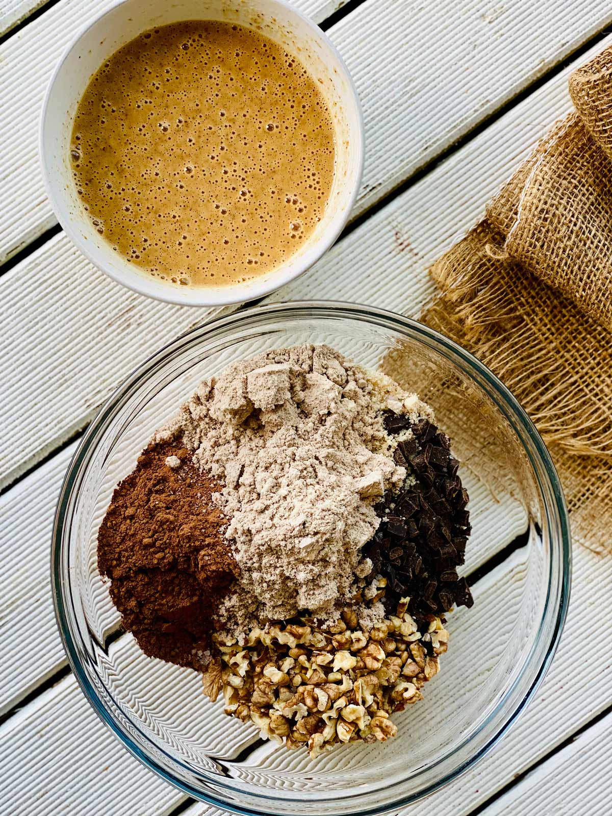 Ingredients for easy protein brownies in a glass bowl and liquid ingredients in a white ceramic bowl