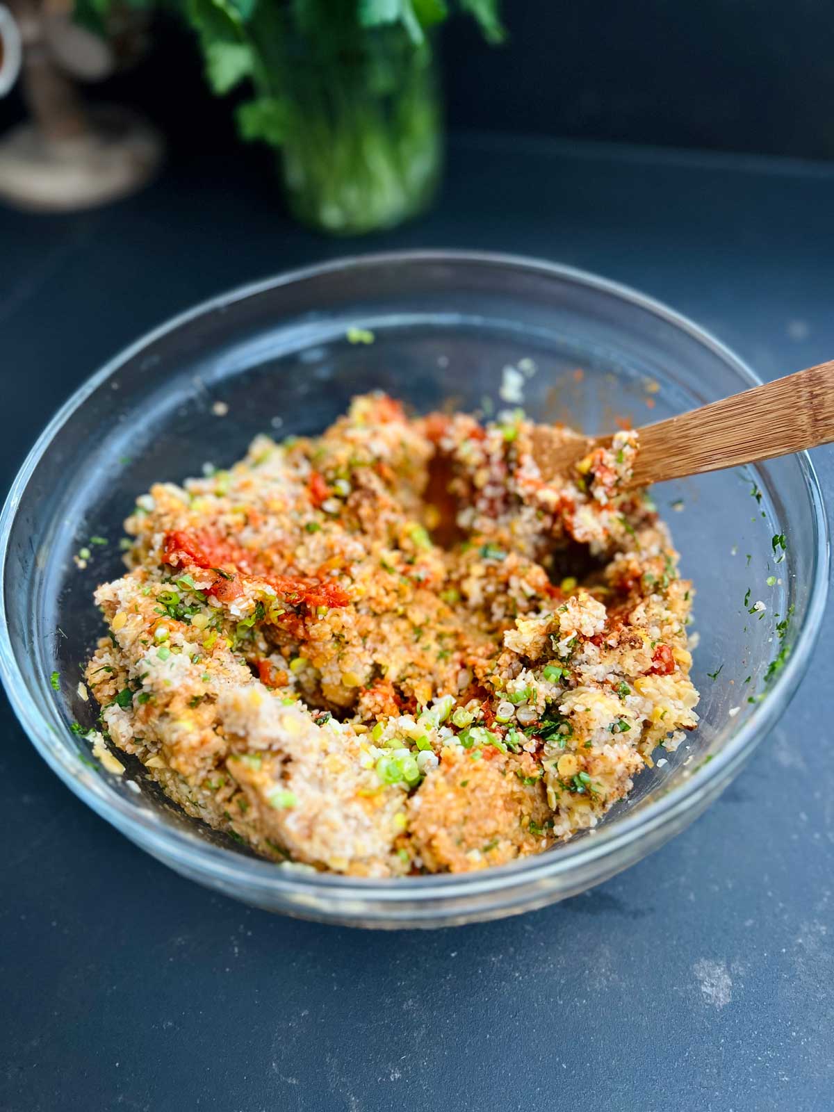 Turkish red lentil meatballs mixture combined with a wooden spoon in a glass bowl