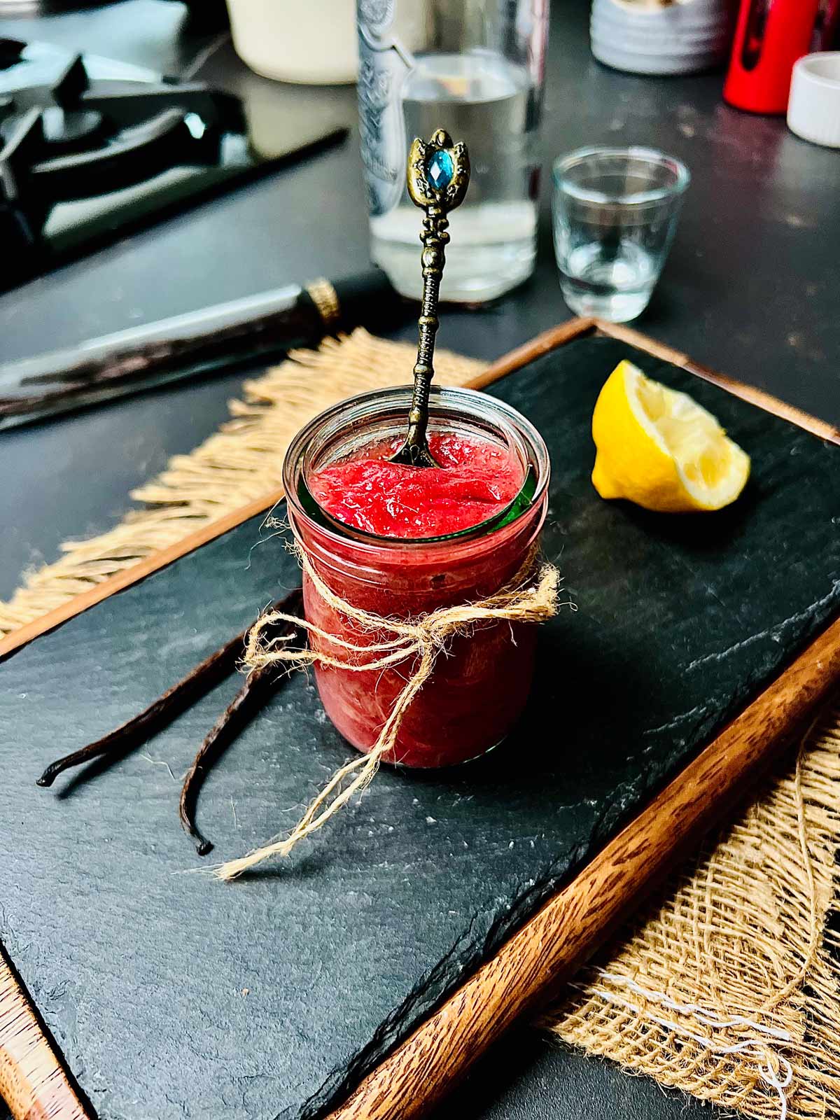 Rhubarb with gin jam in a small jar on a black chalkboard with wooden frame and a fancy teaspoon tucked in.