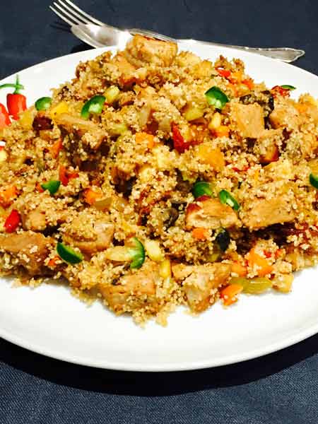 A white plate with delicious couscous, mixed with chunks of roast pork.