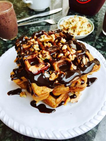 A white plate with scrumptious waffles, all covered in delicious chocolate sauce.
