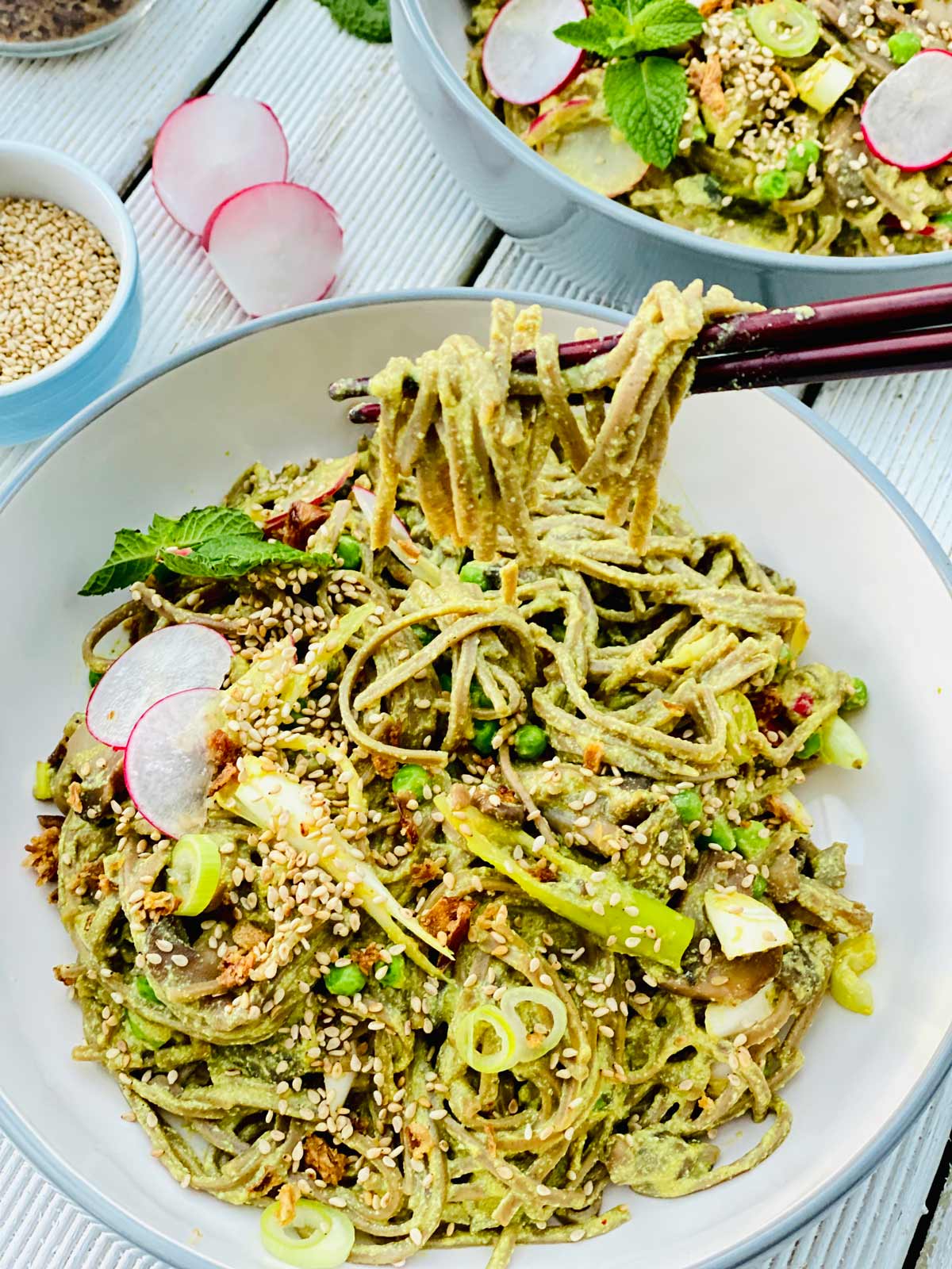 Silken tofu pasta dish in a white and gray rim deep plate and chopsticks tucked in with 2 radish slices, scallions and sesame seeds sprinkled over