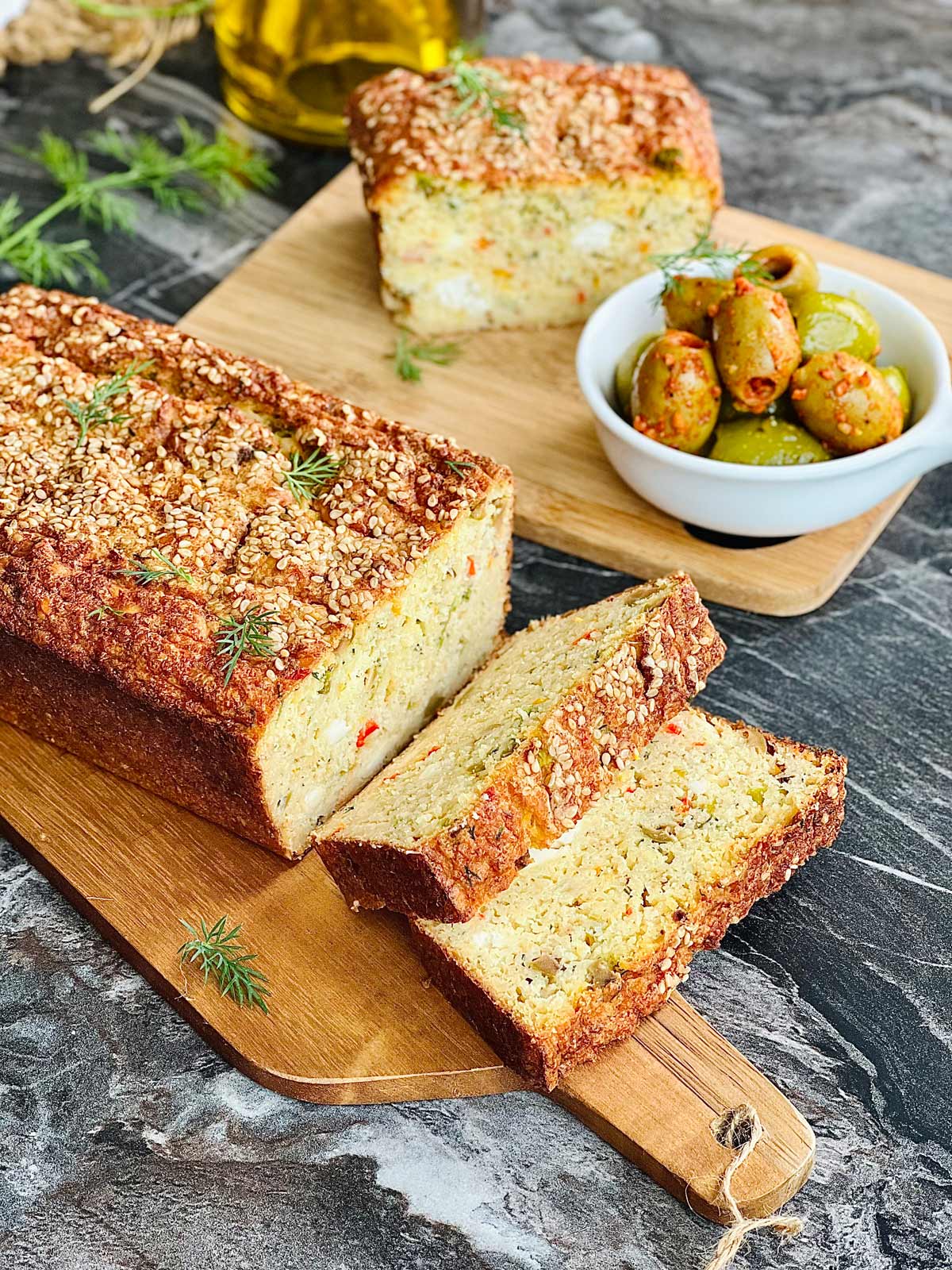 Sliced lentil bread on a wooden chopping board and further away another piece of lentil bread and olives on a wooden board.