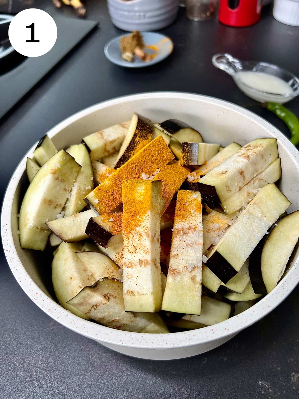 Slices of aubergine with turmeric powder ready to be coated in an off white pot.
