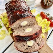 Smoked meatloaf on a wooden chopping board with salad and tomatoes around it.