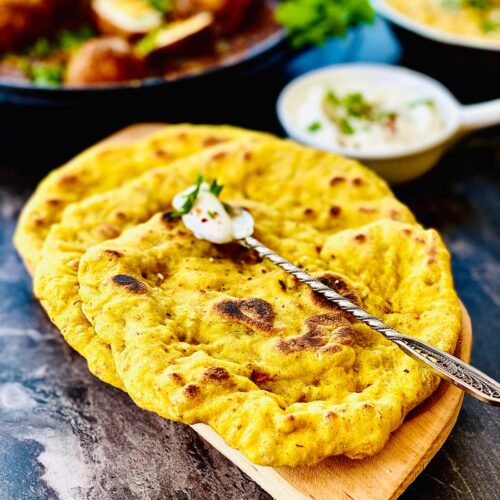 Sourdough naan on a wooden board with yoghurt in a silver spoon on top