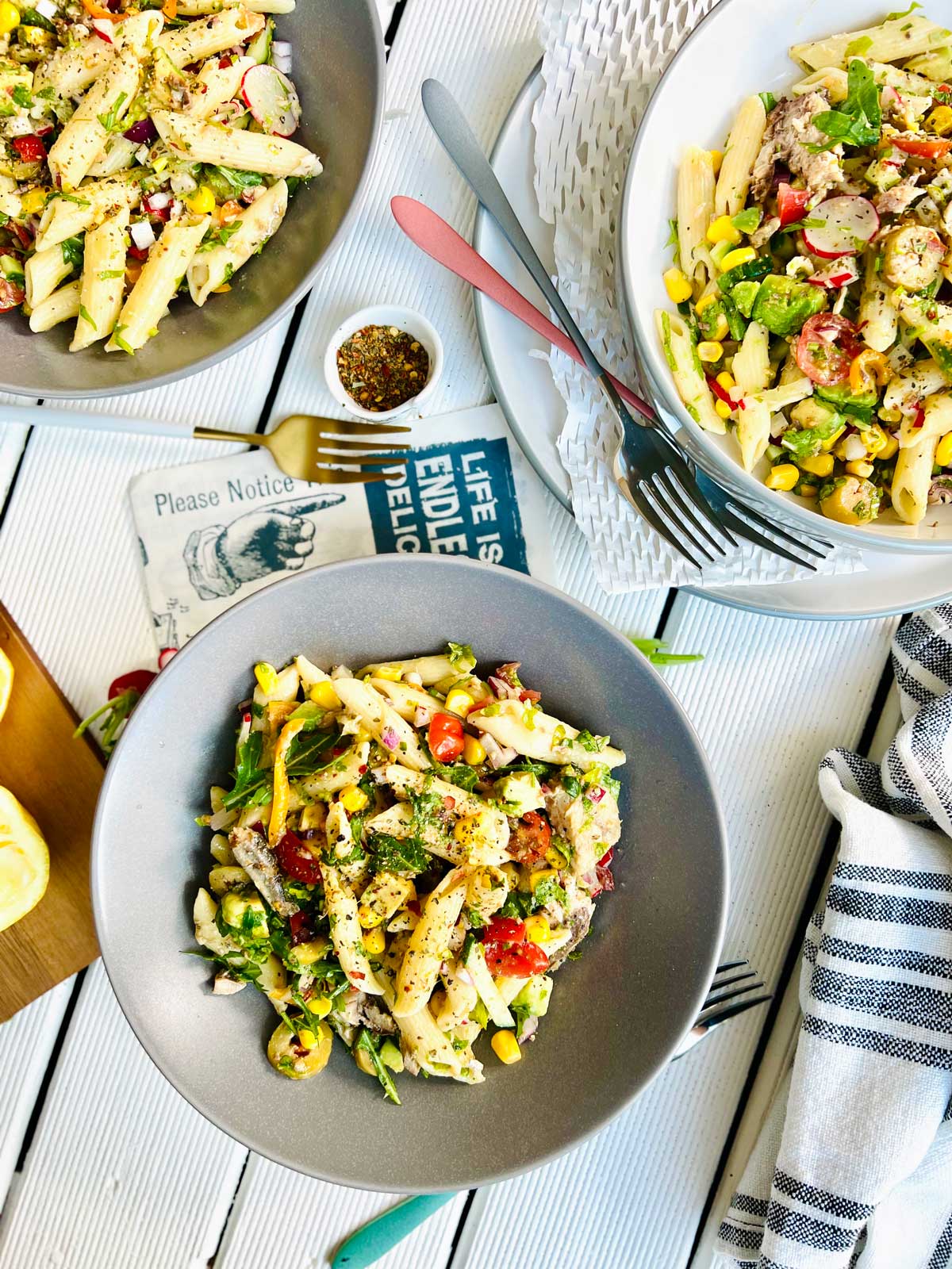 Bird’s eye view of three grey plates half filled with colourful pasta penne and spanish sardines