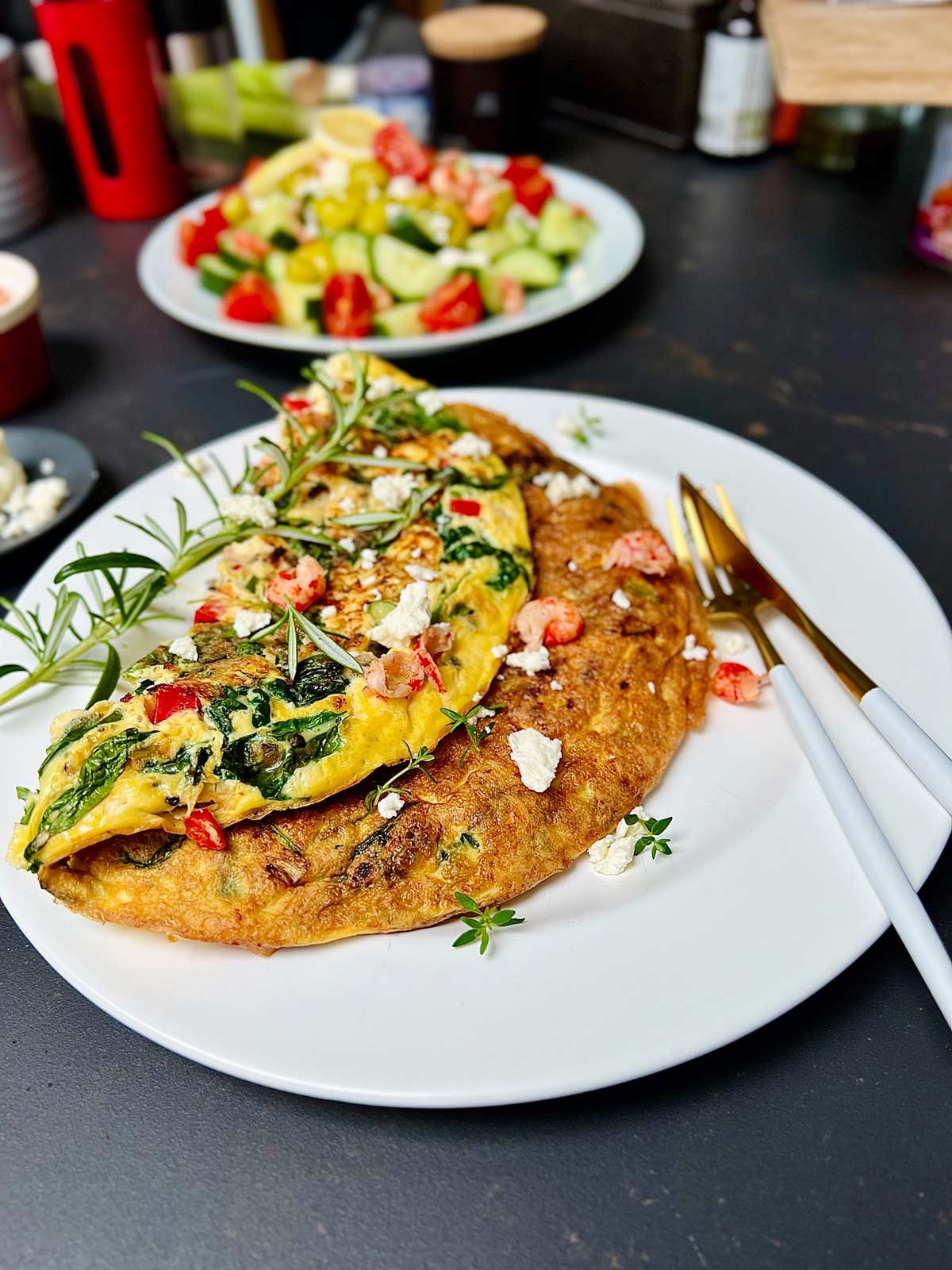 Feta and spinach omelette on a white plate with a golden cutlery and some herbs sprinkled.