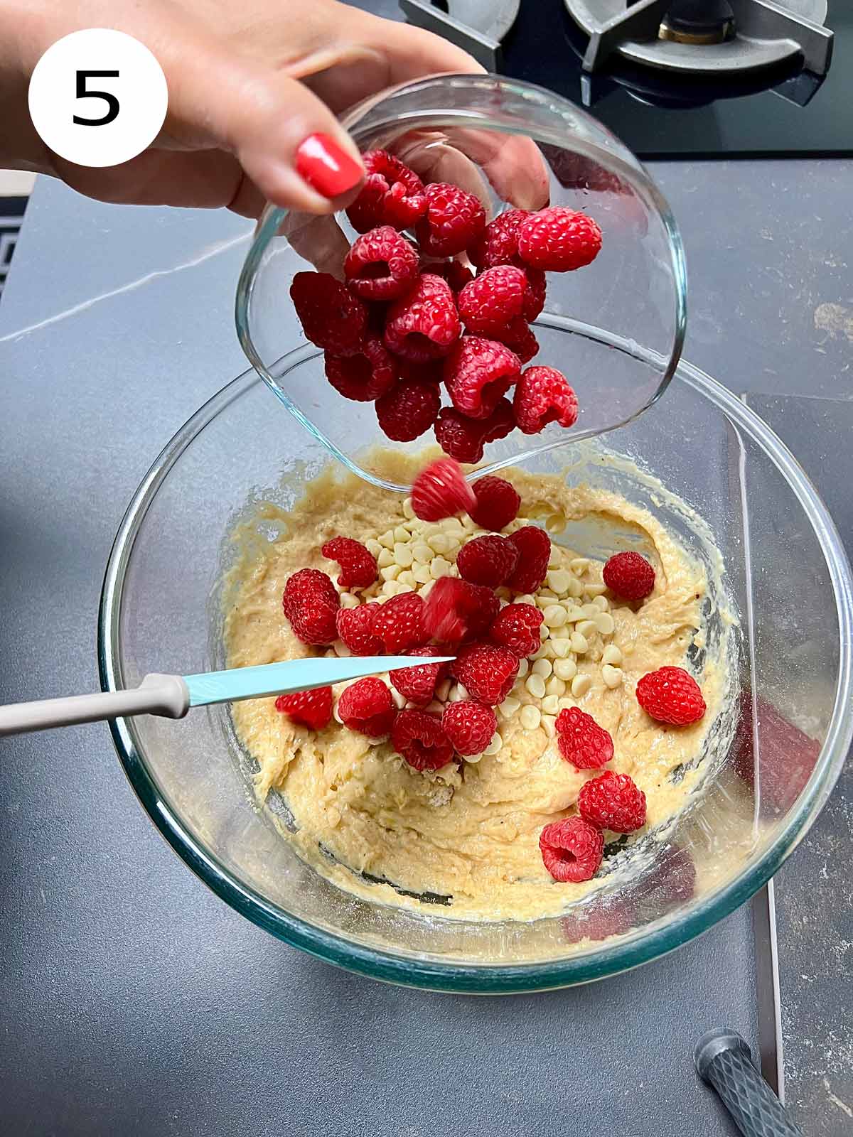 Strawberries in a small glass bowl being added to the white chocolate raspberry muffin batter.