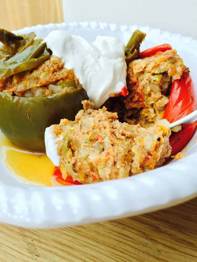 A split stuffed pepper with cream topping, on a white plate and a spoon tucked in.