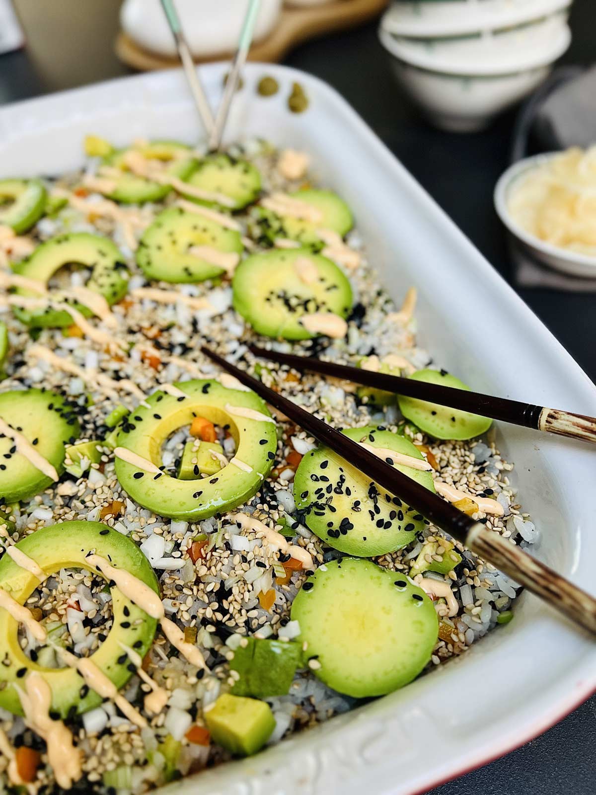 Close up of sushi bake topped with avocado slices and chopsticks tucked in.