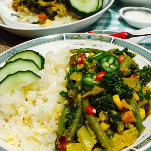 A white plate of scrumptious vegetarian Thai curry, together with egg-fried rice and other veggies.