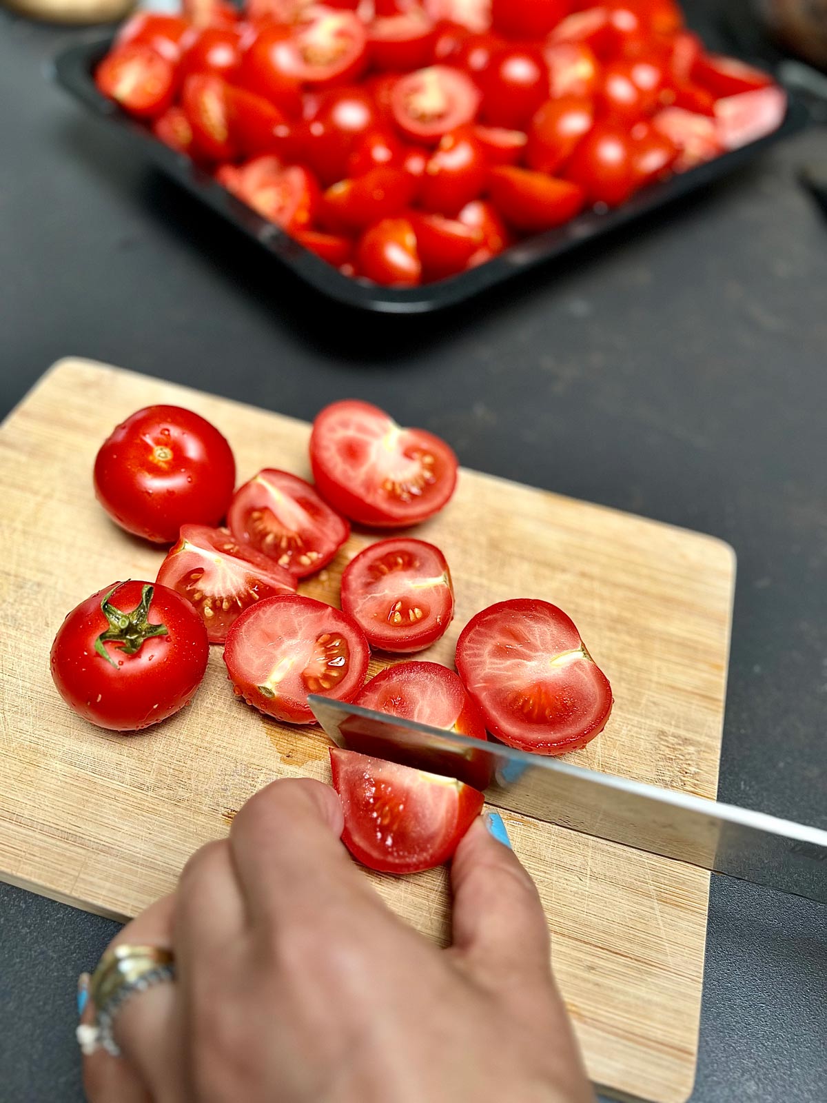 Whole tomatoes, halves and quarters on a wooden chopping board being prepared to make passata.