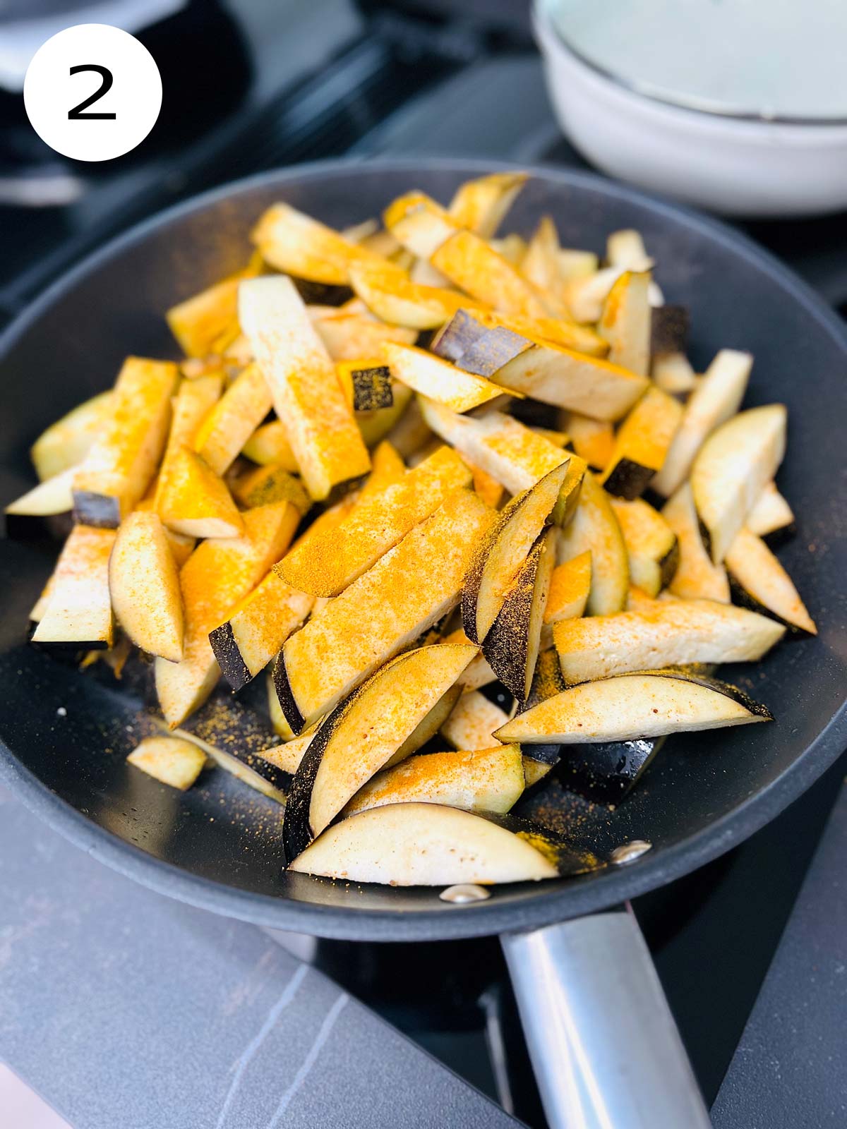 Turmeric coated aubergine pieces in a pan ready to be shallow fried.