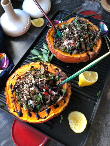 Two kabucha stuffed squash halves -birds-eye on a griddle plate with two half lemons and forks tucked in with a hefty drizzle of reduced balsamic vinegar