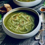 Wild garlic and nettles soup with cream swirls and red chilli flakes sprinkled on top on a marbled worktop