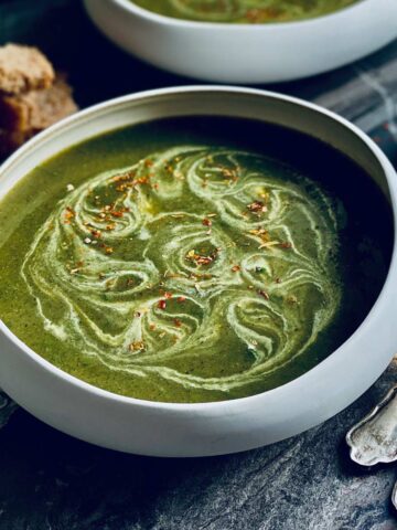 Wild garlic and nettles soup with cream swirls and red chilli flakes sprinkled on top on a marbled worktop