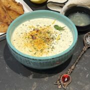 Yoghurt mint sauce in a green serving bowl and spices sprinkled over.
